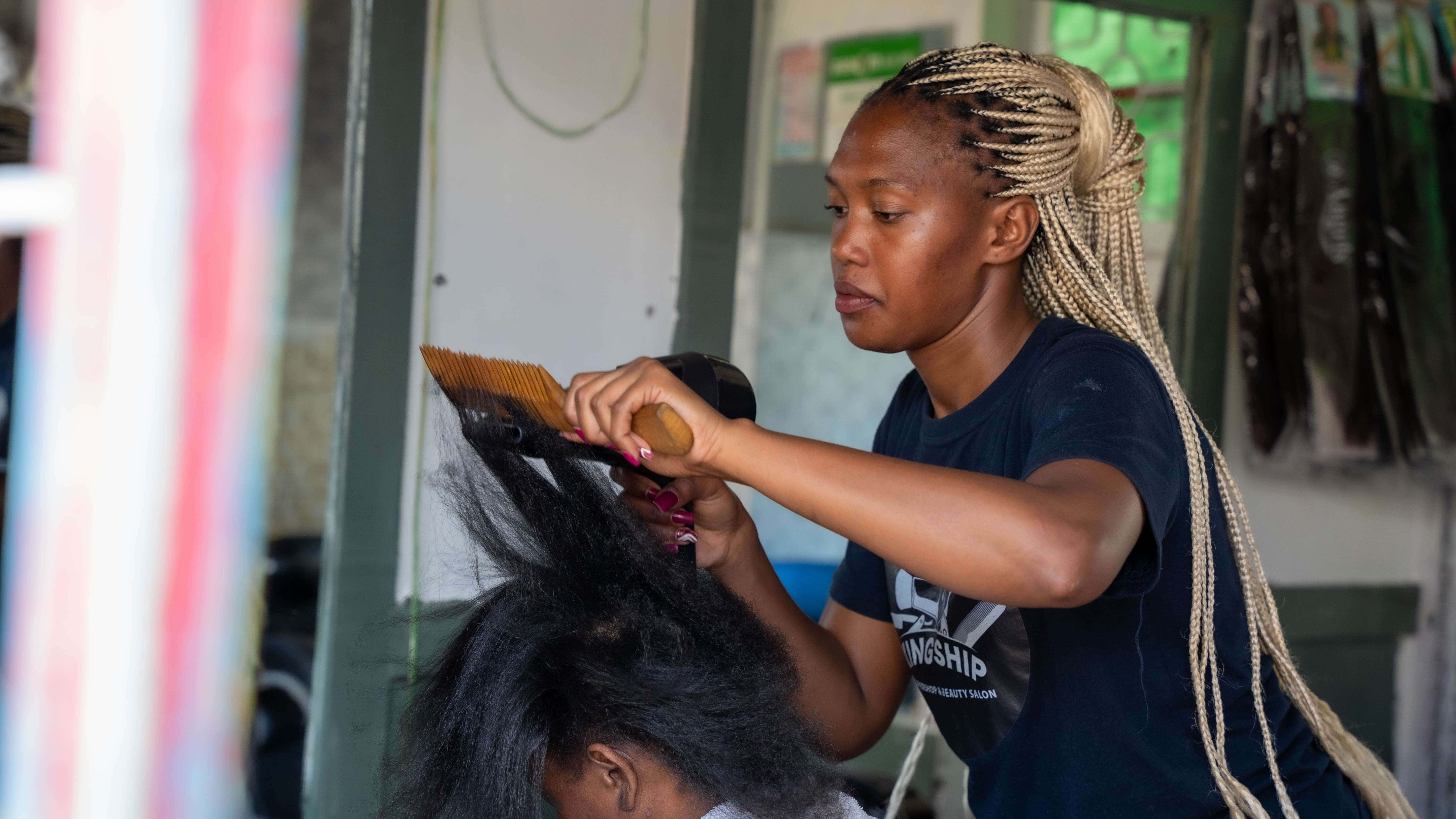 Mitchelle Nthambi blow dries hair of a client before starting to braid it at her salon in Utawala. Mitchelle received a business grant from the IRC & IKEA Foundation’s Re:BUiLD program