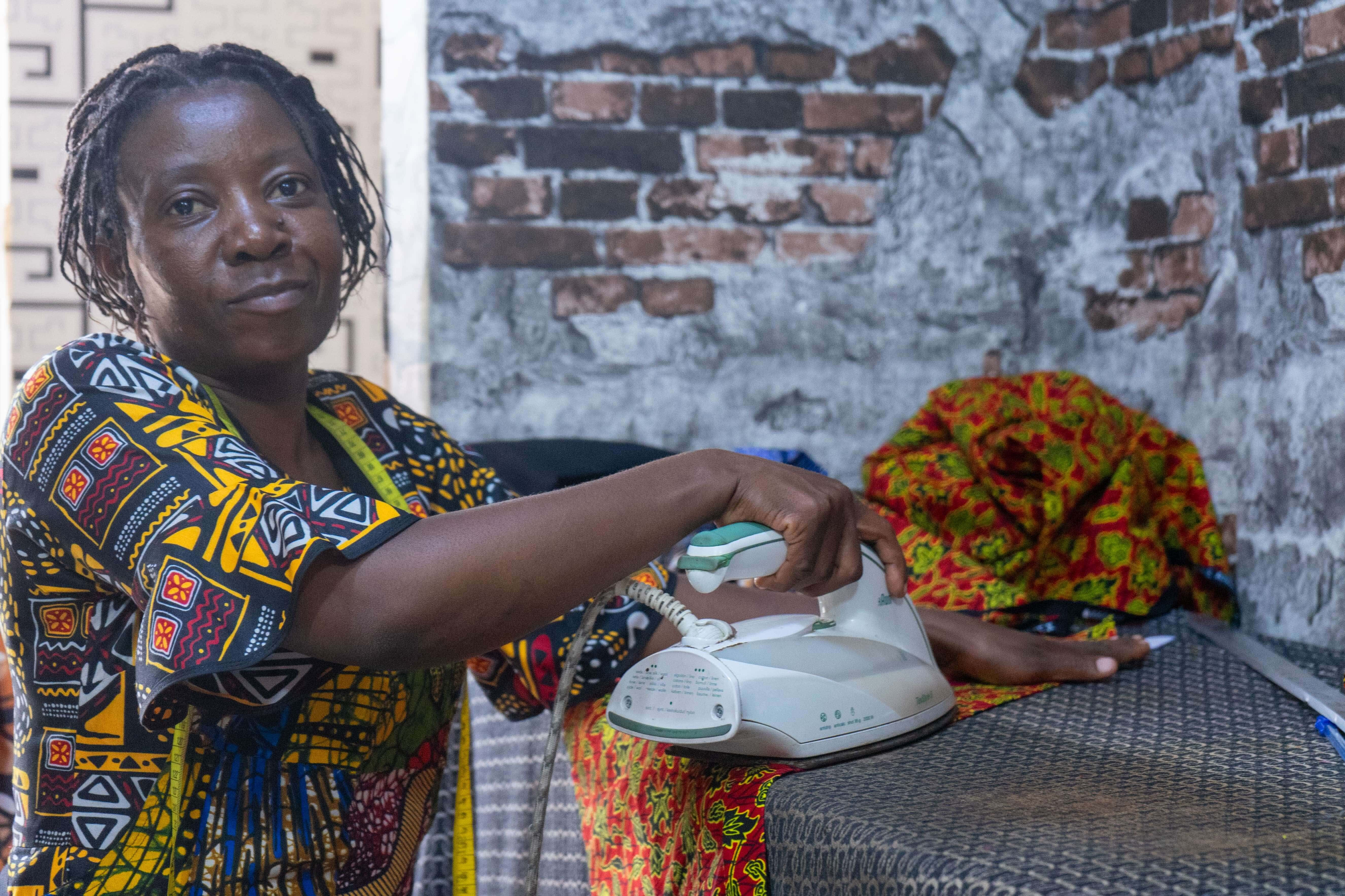 Riziki Kajabika at her sewing desk in Kampala.  She received a business grant as part of the IRC’s Re:BUiLD Program Wave 1 RCTs grant, bought a sewing machine, fabric and paid rent for her shop.